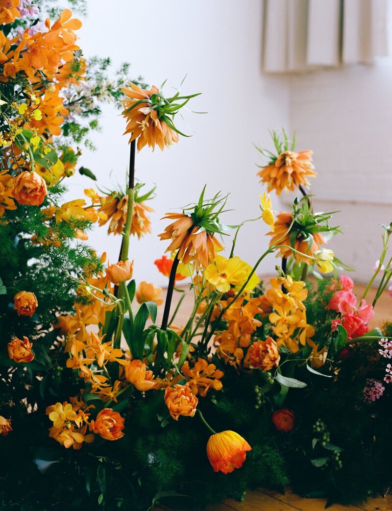 Film photo of a dramatic wedding floral installation featuring vibrant yellow, orange, and coral-toned blooms with dynamic movement and texture — styled by a floral designer and photographed by a film wedding photographer.