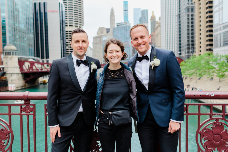 A photo of photographer Shelby Shenkman posing on a bridge with two grooms whose wedding she just shot