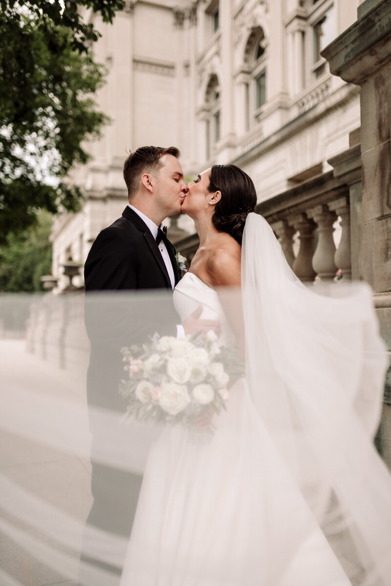 Dramatic veil photo of bride and groom kissing outside Milwaukee public library