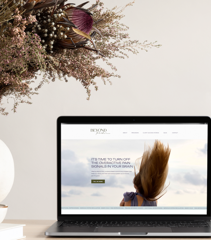 Website designed by Roberta open on a laptop with a bunch of flowers on the table beside it