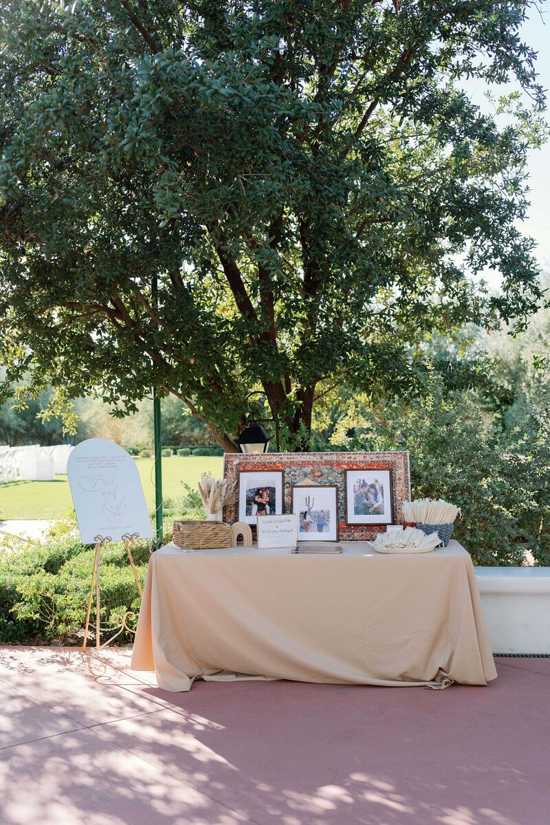 Welcome table at a wedding with beige linens, picture frames, and guest favors.