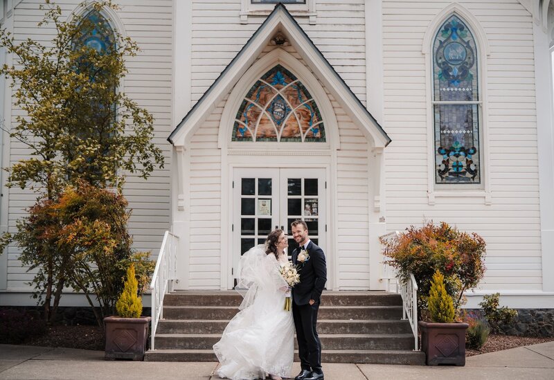a bride and groom smiling outside of a church on their wedding day