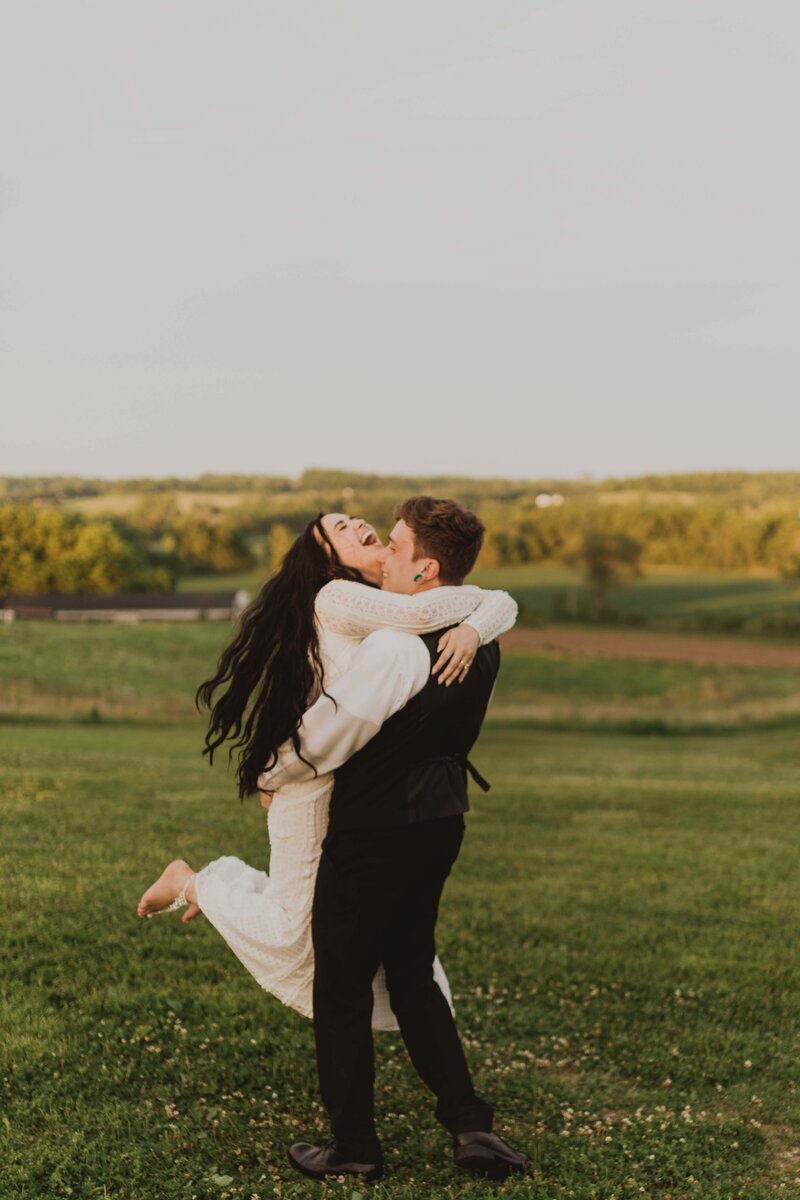 Groom swinging bride around while bride throws head back and laughs.