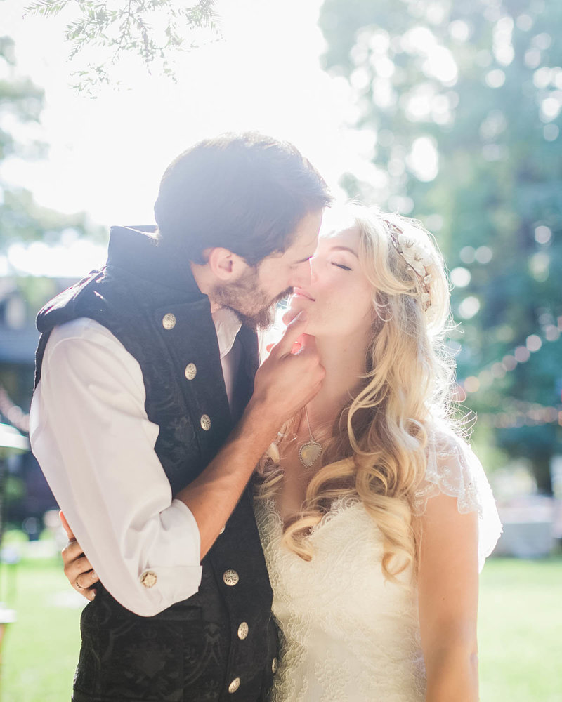 Light filters through while Groom holds Brides chin leaning in to kiss her