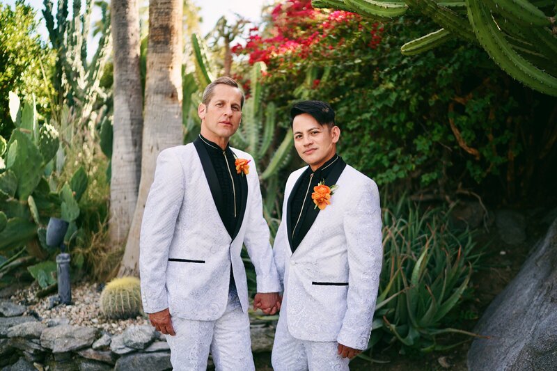 A couple in white suits holding hands.