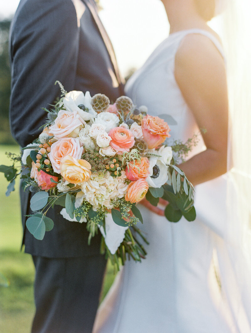 sunsoaked couple at wedding holding beautiful white and peach bouquet