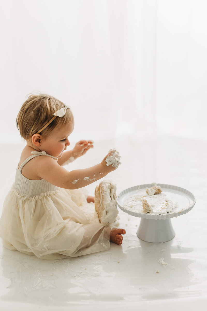Cake smash with neutral colored outfits and cake falling on floor as baby is eating cake