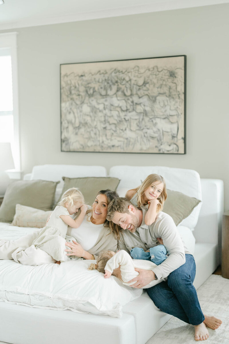 mother and father play with a pile of children on their white bed