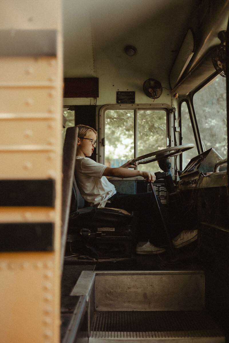 A young boy on a school bus pretending to drive. 
