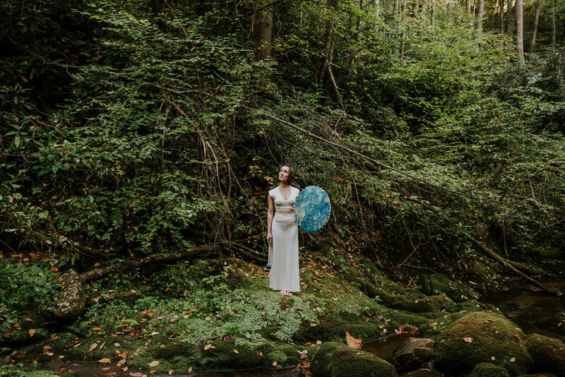 woman standing in a lush forest, holding a blue drum