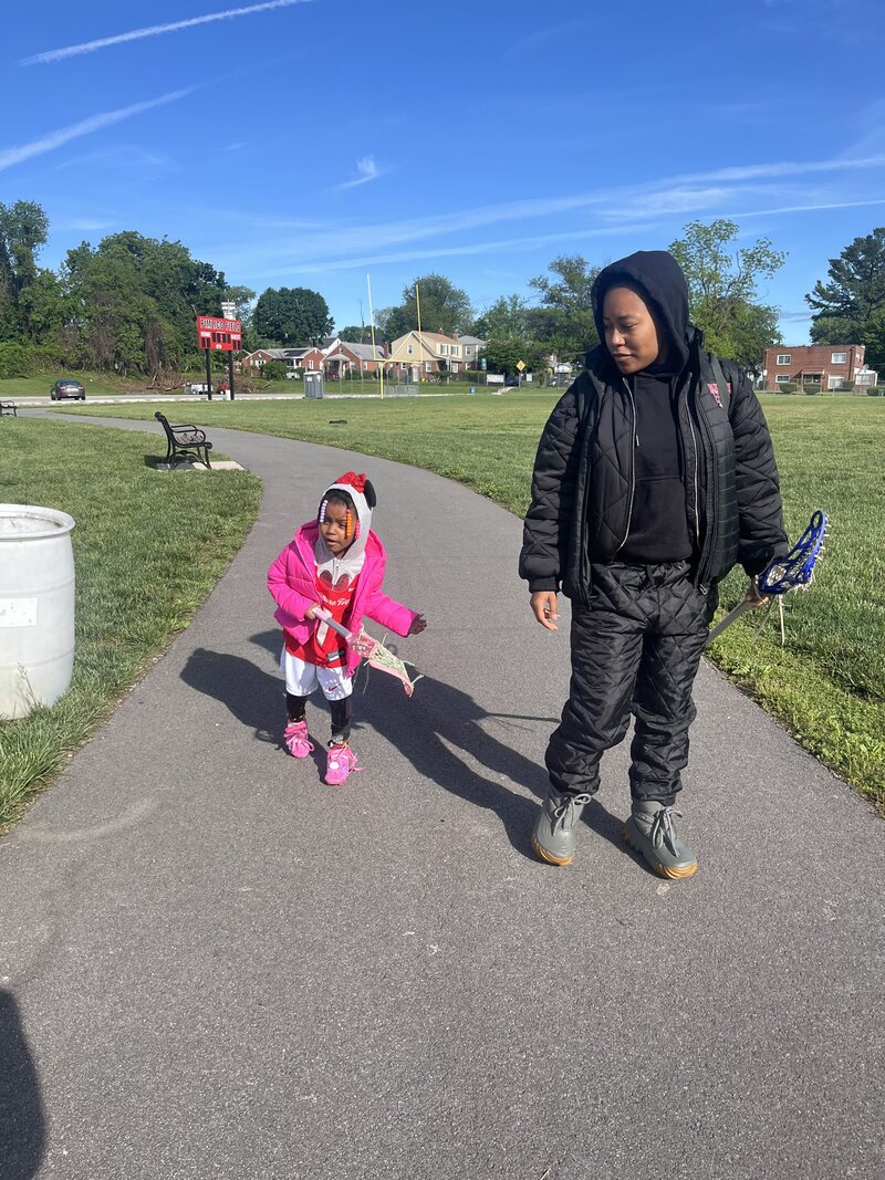 Photo of young girl ready to play lacrosse with her mom, also holding lacrosse stick