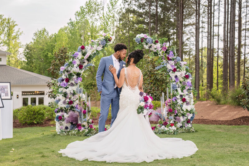 Bride and groom sharing a romantic moment under a floral wedding arch at a luxury outdoor wedding in Raleigh, NC.