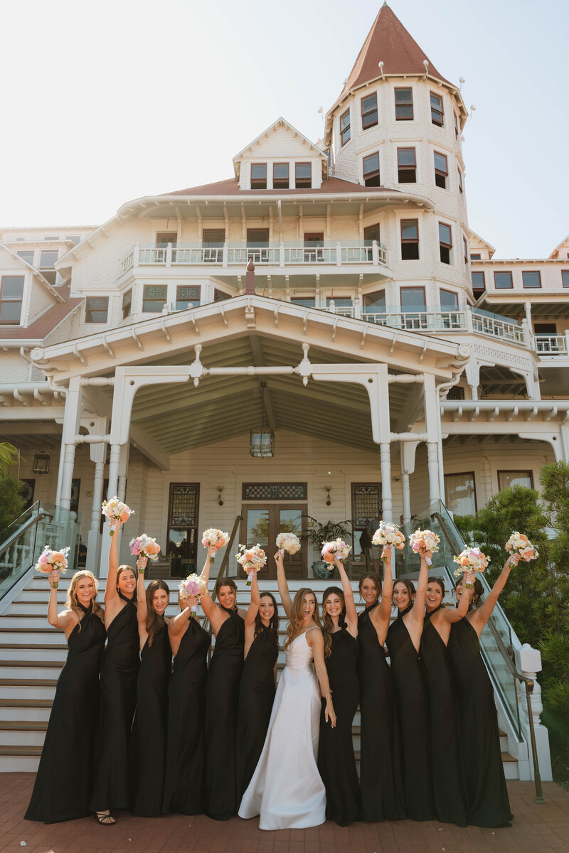 a group of bridesmaids and a bride laughing and cheering in front of a hotel