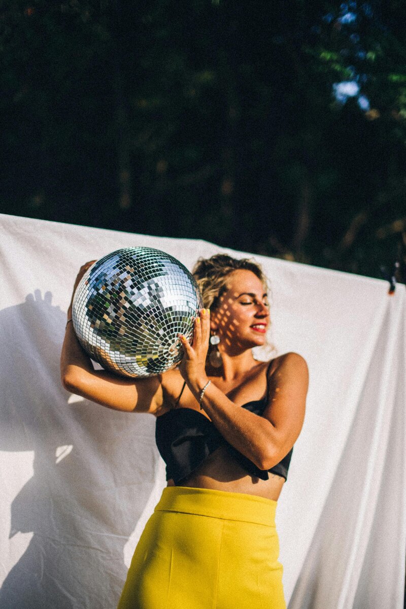 Woman holding a disco ball on her shoulder smiles thinking about the results a pinterest strategy will do for her small online business