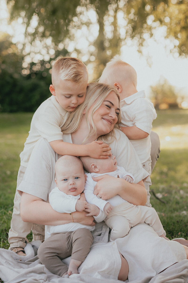 Photo of a mom with her 4 young boys, her toddler boys standing beside her and her twin babies in her arms taken by a langley photographer