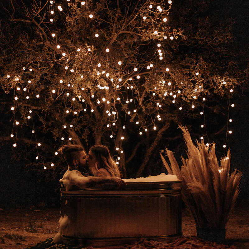 couple kisses in metal bath tub with pampas grass and fairy lights