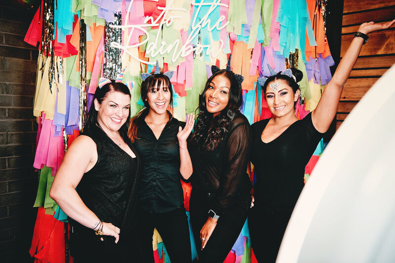 Group of coworkers posing with unicorn ears in front of a rainbow fringe backdrop—captured at a Phoenix corporate photo booth activation by MISGIF.