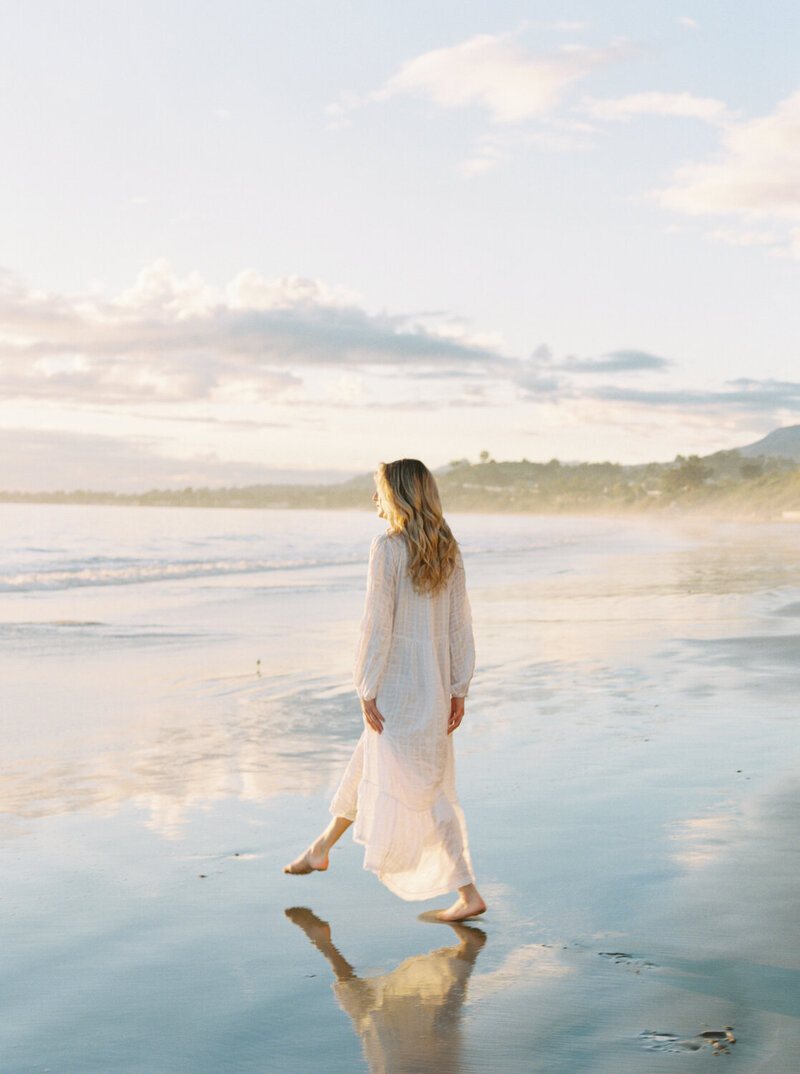 engaged woman in satin romper standing on beach
