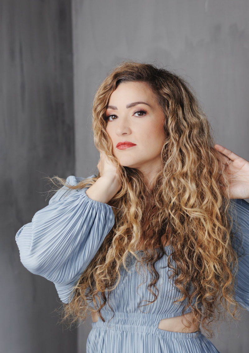 Portrait of woman with long curly blonde hair and bold makeup wearing a blue top