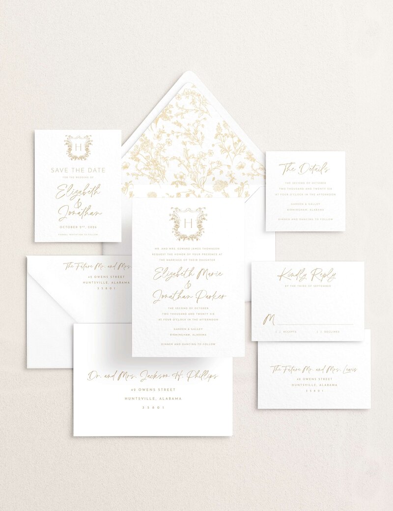 Flat lay of an elegant wedding invitation suite with floral details and champagne colored ink.