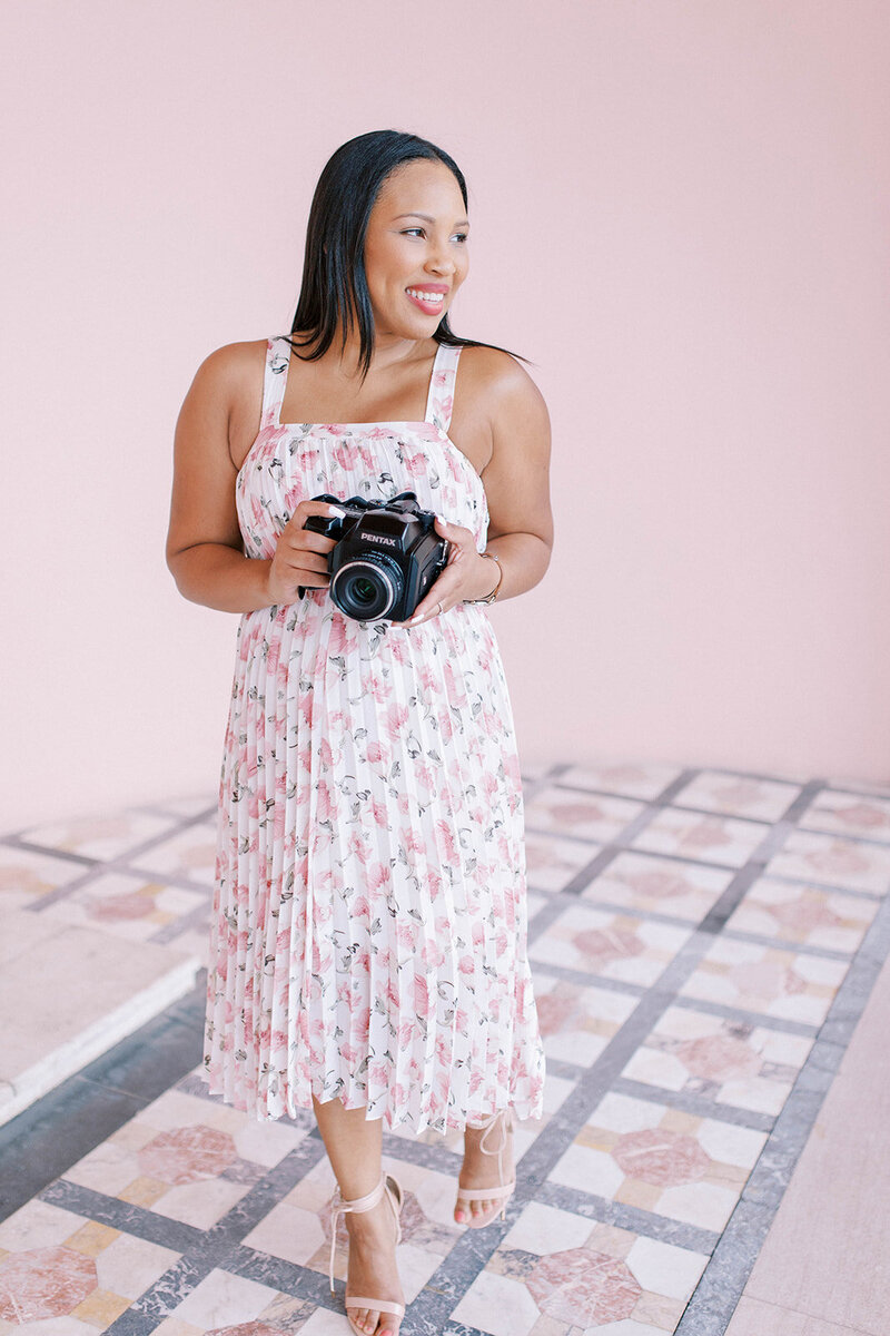 woman holding camera wearing pink floral dress at branding session in Florida