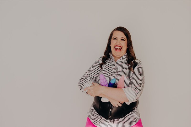 woman in striped white and black shirt holding various colorful sex toys in her right hand