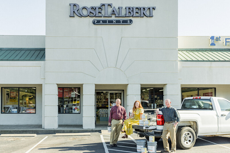 Local business owners stand outside Rose Talbert Paints in Columbia, SC, posing beside a white pickup truck loaded with paint buckets. The storefront features bold signage and large windows displaying supplies. The team’s friendly expressions and relaxed poses highlight their commitment to quality and service. Small business branding photography in Columbia, SC, capturing local entrepreneurs and family-owned businesses.