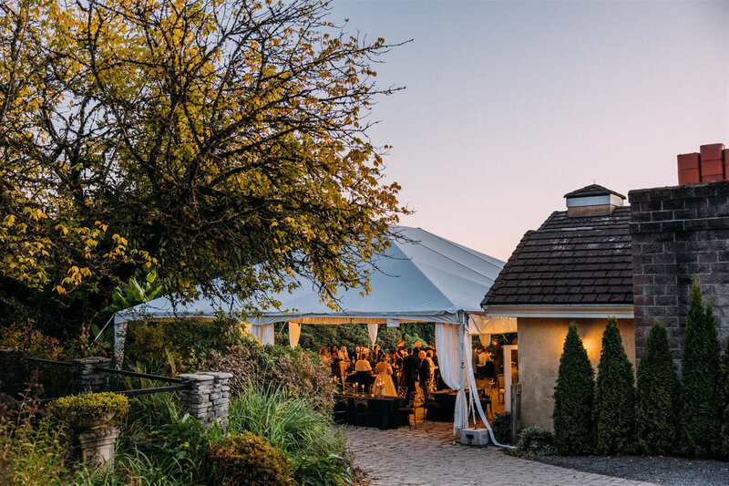 Evening view of an elegant tented event with warm lights and lush greenery