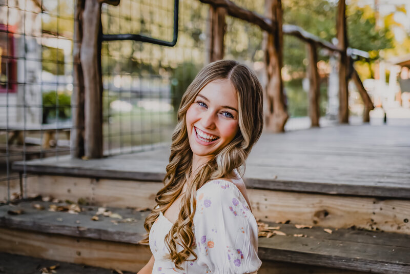 High school senior in floral dress sitting on steps during session in Gruene, TX.