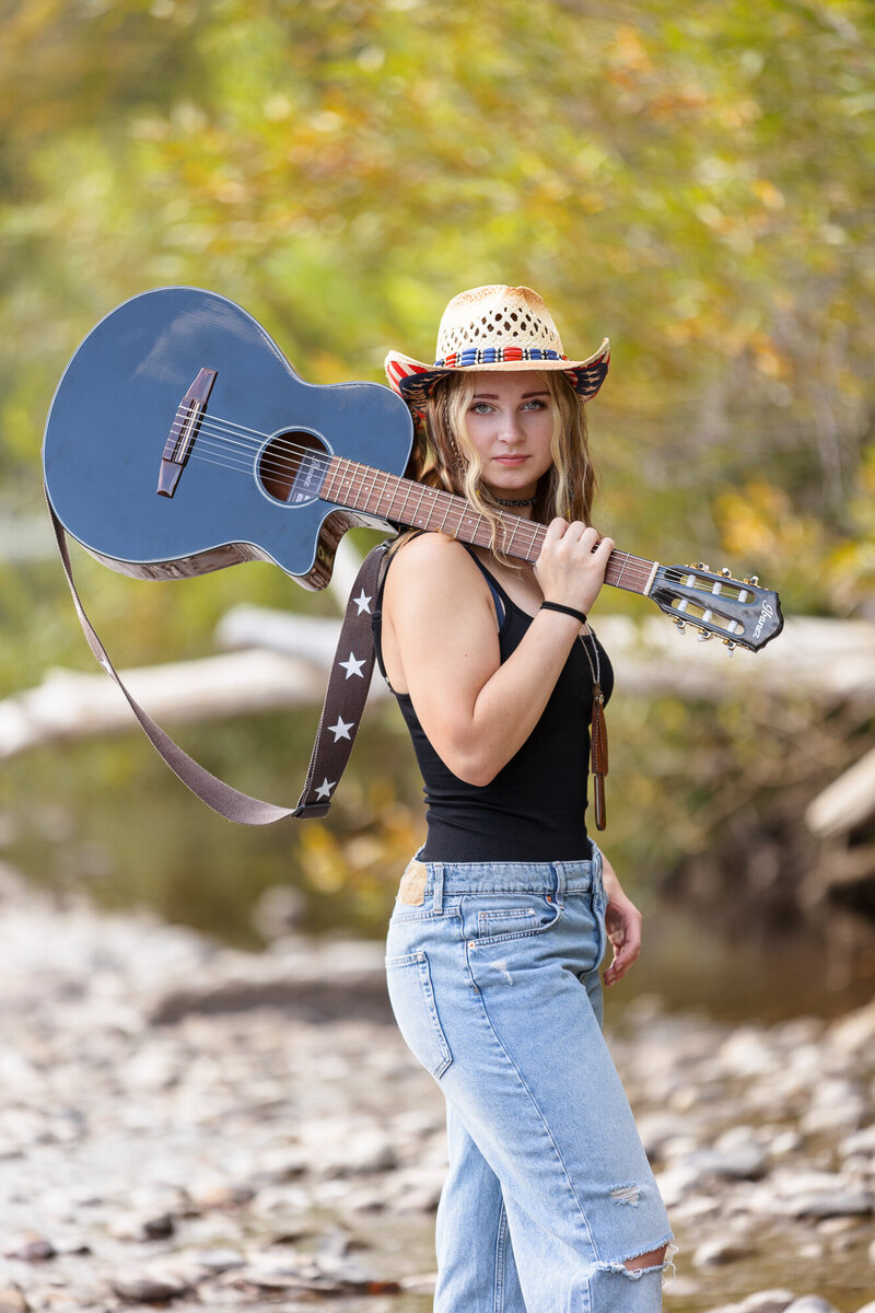 Senior girl standing and holding a guitar at the Boise River.
