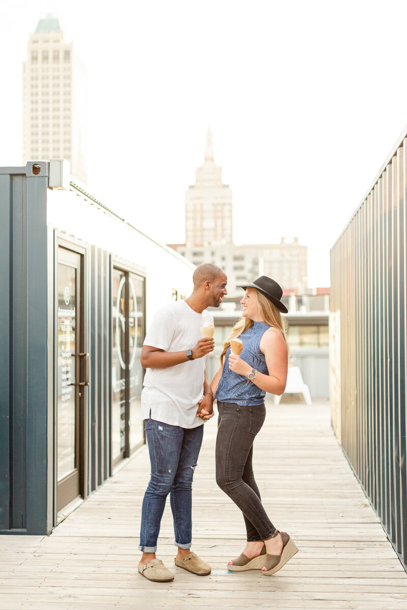 A couple enjoying Rose Rock  ice cream during their engagement session, with downtown Tulsa  as their backdrop.