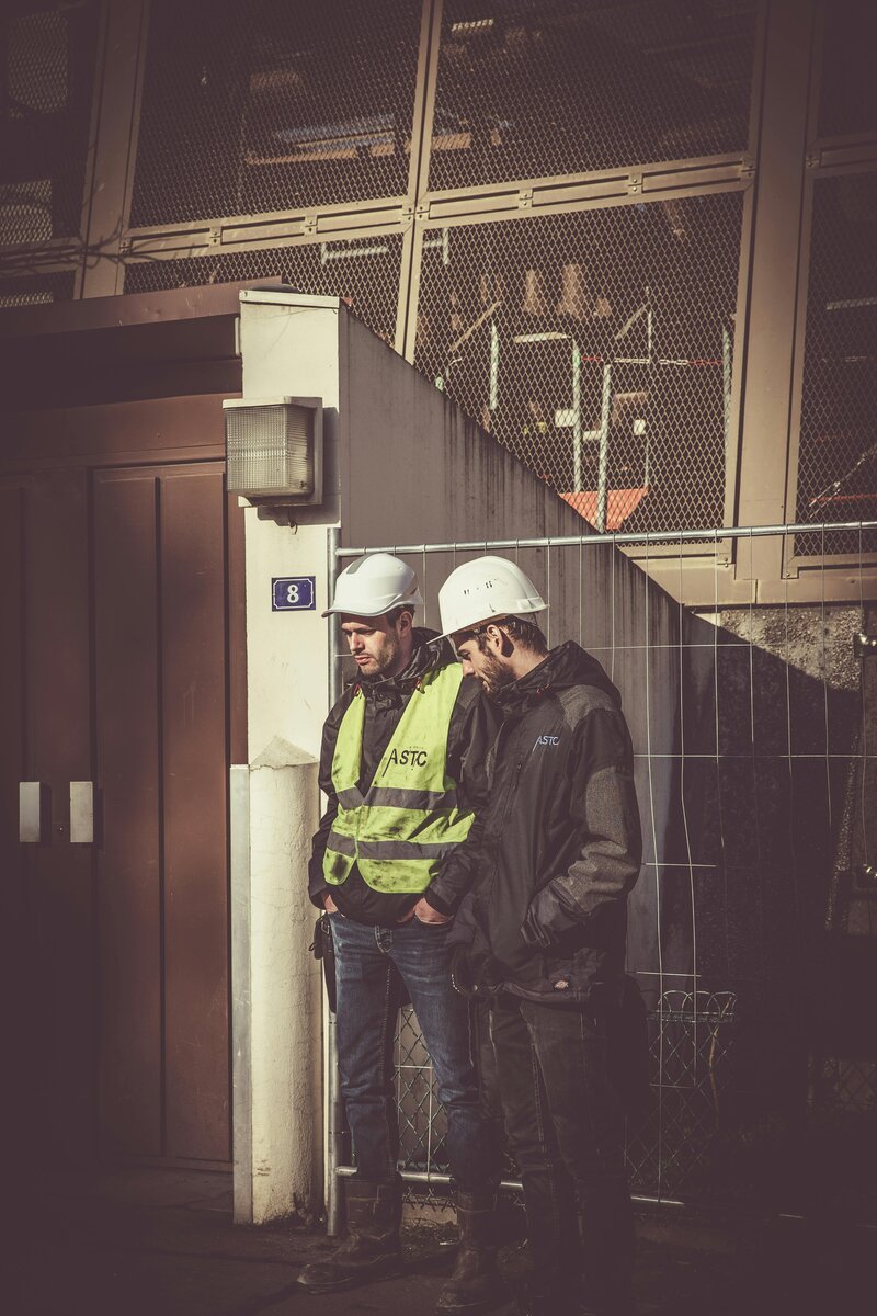 Two industrial workers in hard hats, one appearing disengaged and withdrawn