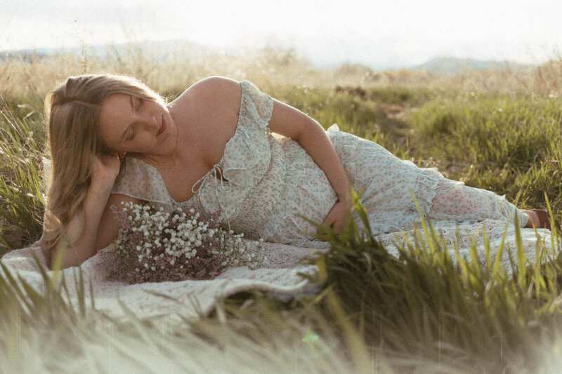 Pregnant mother laying in a field wearing a cottage core dress at sunset.