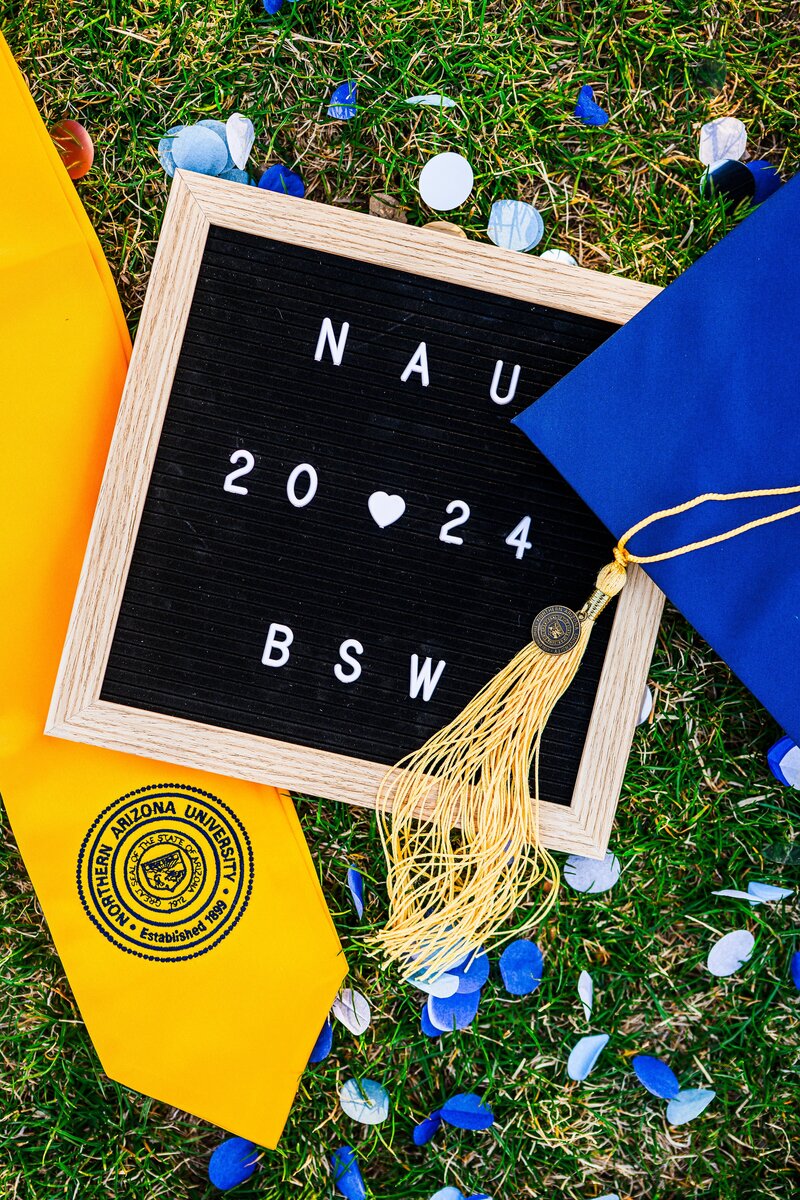 NAU sign with cap and stole on grass with blue confetti at Old Main at Northern Arizona University