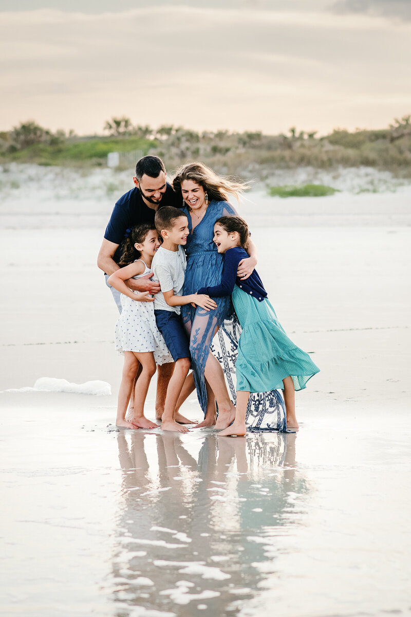 Family of 5 wearing blue and white snuggling and laughing at Hanna Park in Atlantic Beach, FL.