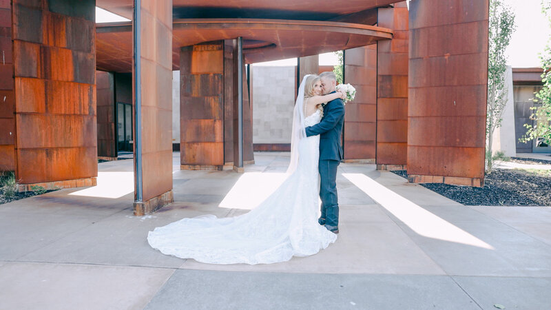 Bride and groom hugging with red modern columns in front of Promontory Club, Park City Utah by Cali Warner Media