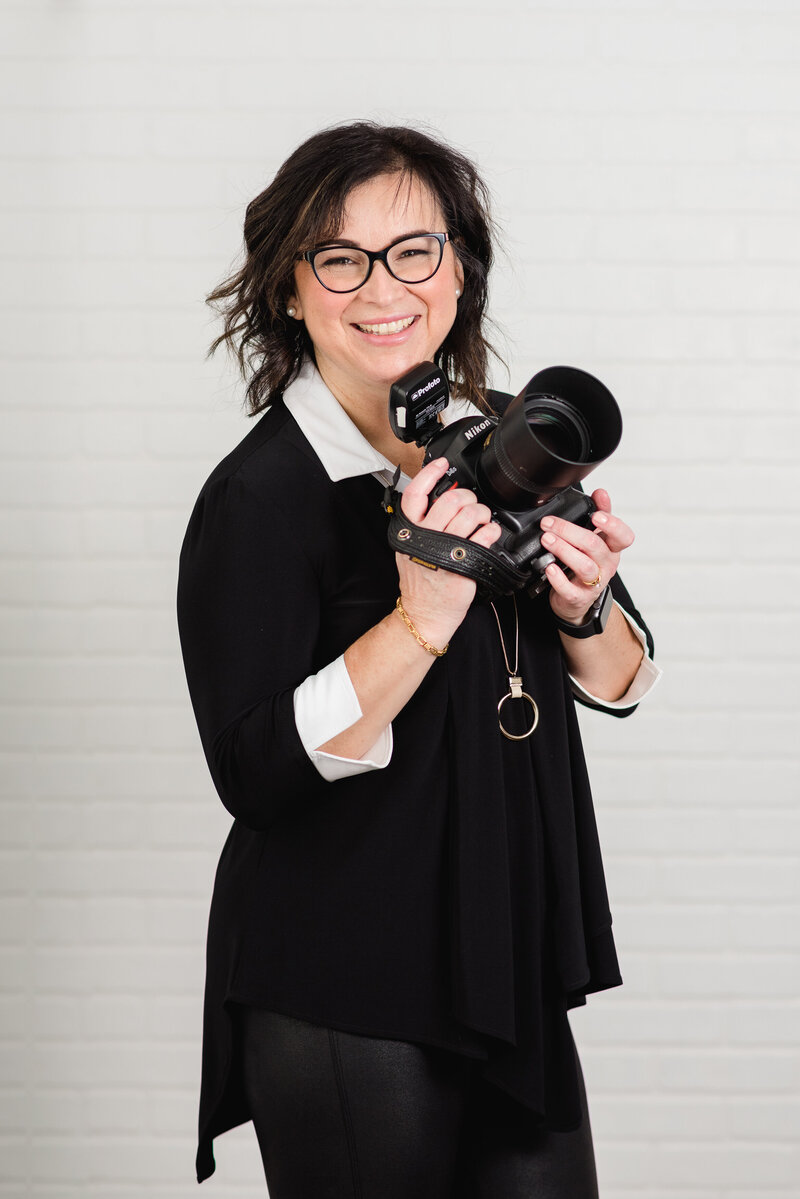 a photo of photographer Elenora Luberto JEMMAN Photography COMMERCIAL taken in studio.  She's wearing a black outfit and is holding her camera