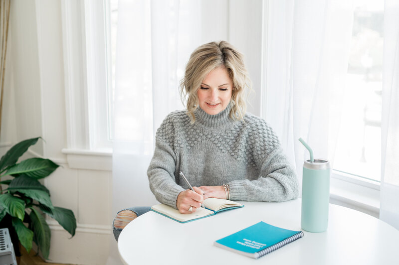 Julie Ladimer, owner of Ladimer Law sitting at a desk in a grey sweater writing in a notebook