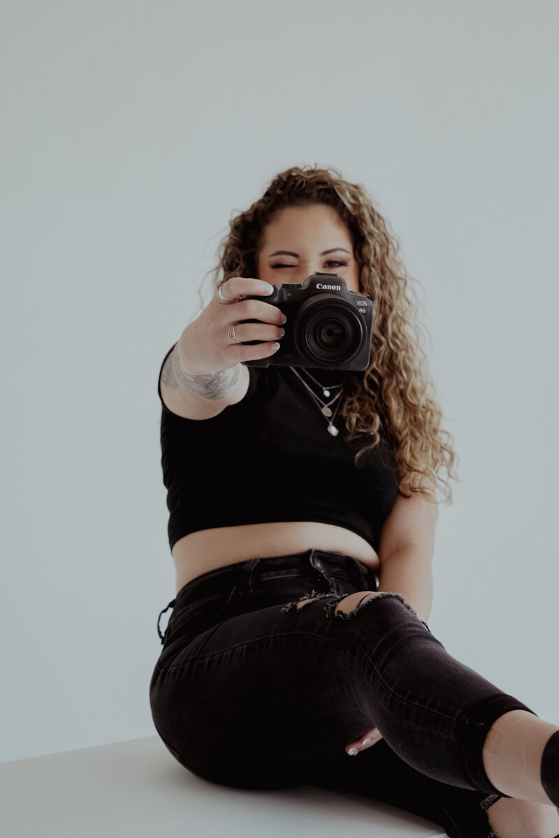 Female photographer holding camera in yellow shirt curly hair