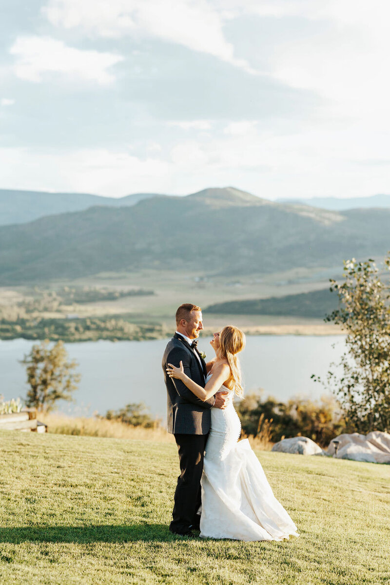 A wedding couple hugging and laughing in front of a mountain lake.