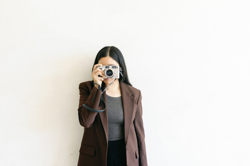 Portrait of stylish women in brown blazer holding a film camera over her eyes