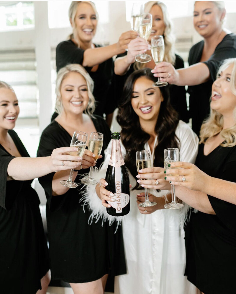 Bride and bridesmaids holding up and cheers glasses of champagne.