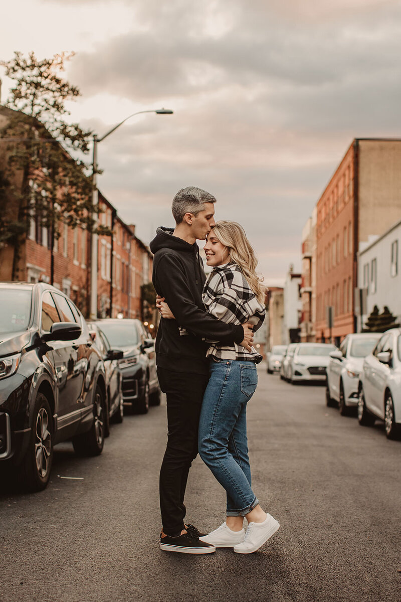 A couple hugging in the middle of the street as one kisses the other's forehead 