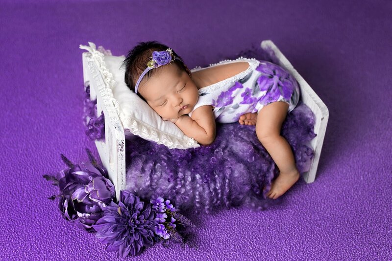 New baby girl in white and purple on a wooden bed at Burnaby photo session