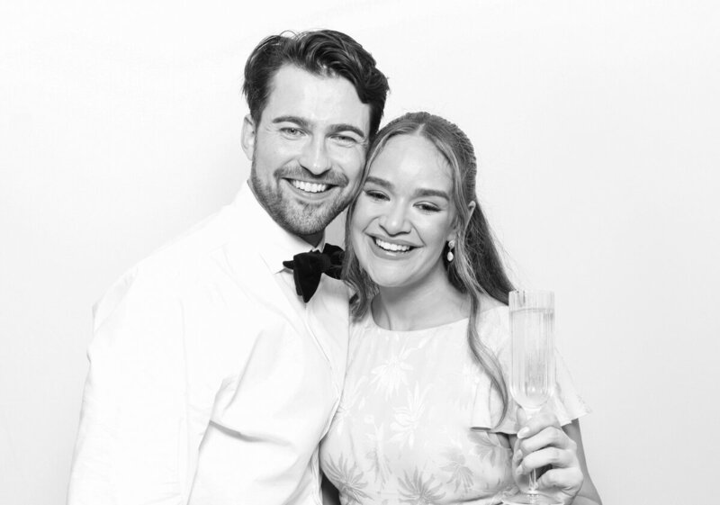 Black and white filter for a couple posing against a white backdrop, during a wedding party entertainment, for Mad Hat Photo Booth at Kin House