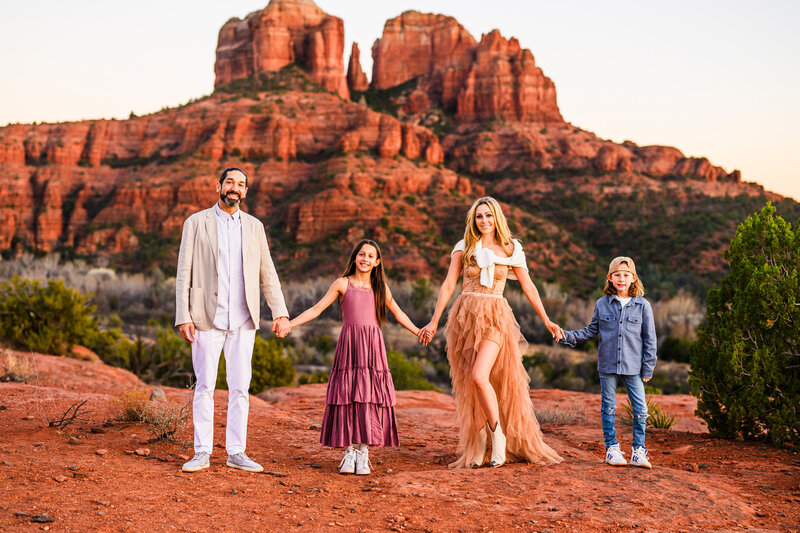 Family in Sedona Arizona holding hands smiling at camera with Cathedral Rock red rock background 