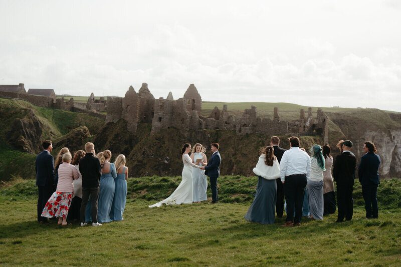 Eloping Ideas | Elopement ceremony with guests on an ocean cliff with a huge castle in the background 