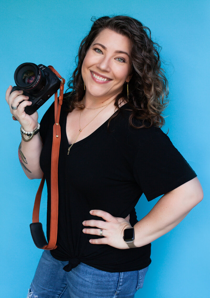 Portrait of Southwest Missouri photographer Dynae Levingston holding her camera in front of a seamless turquoise  backdrop