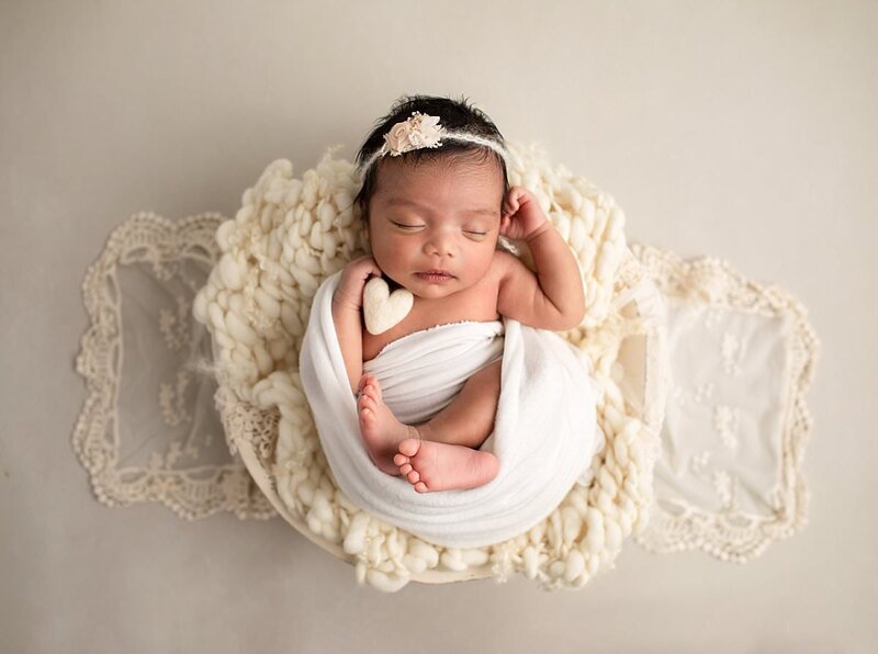 Baby girl swaddled with feet out holding a cream colored heart by Baltimore Newborn Photographer