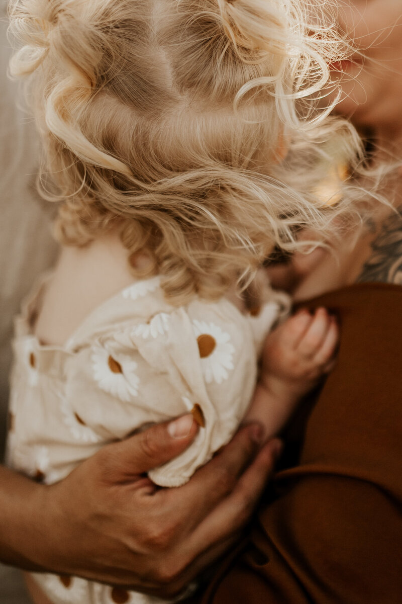 Blonde curly headed toddler being held by her parents.